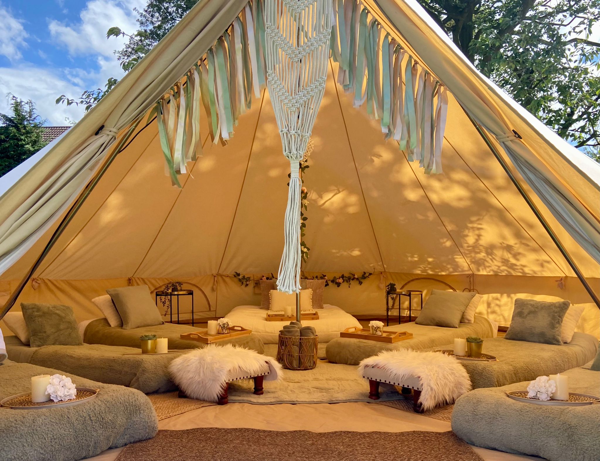 Bell tent hire Cheshire interior styled with sage green cushions and a macramé wall hanging