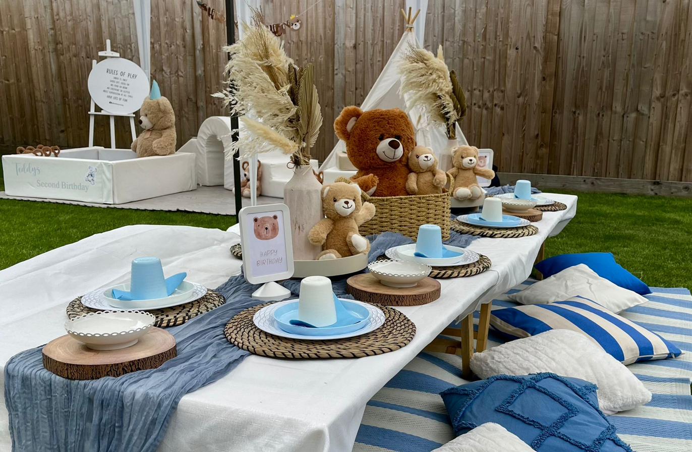 Teddy bear themed party table set up outdoors for a first birthday celebration